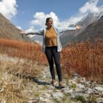 the author standing in beautiful mountains with arms open embracing her long writing and travel journey